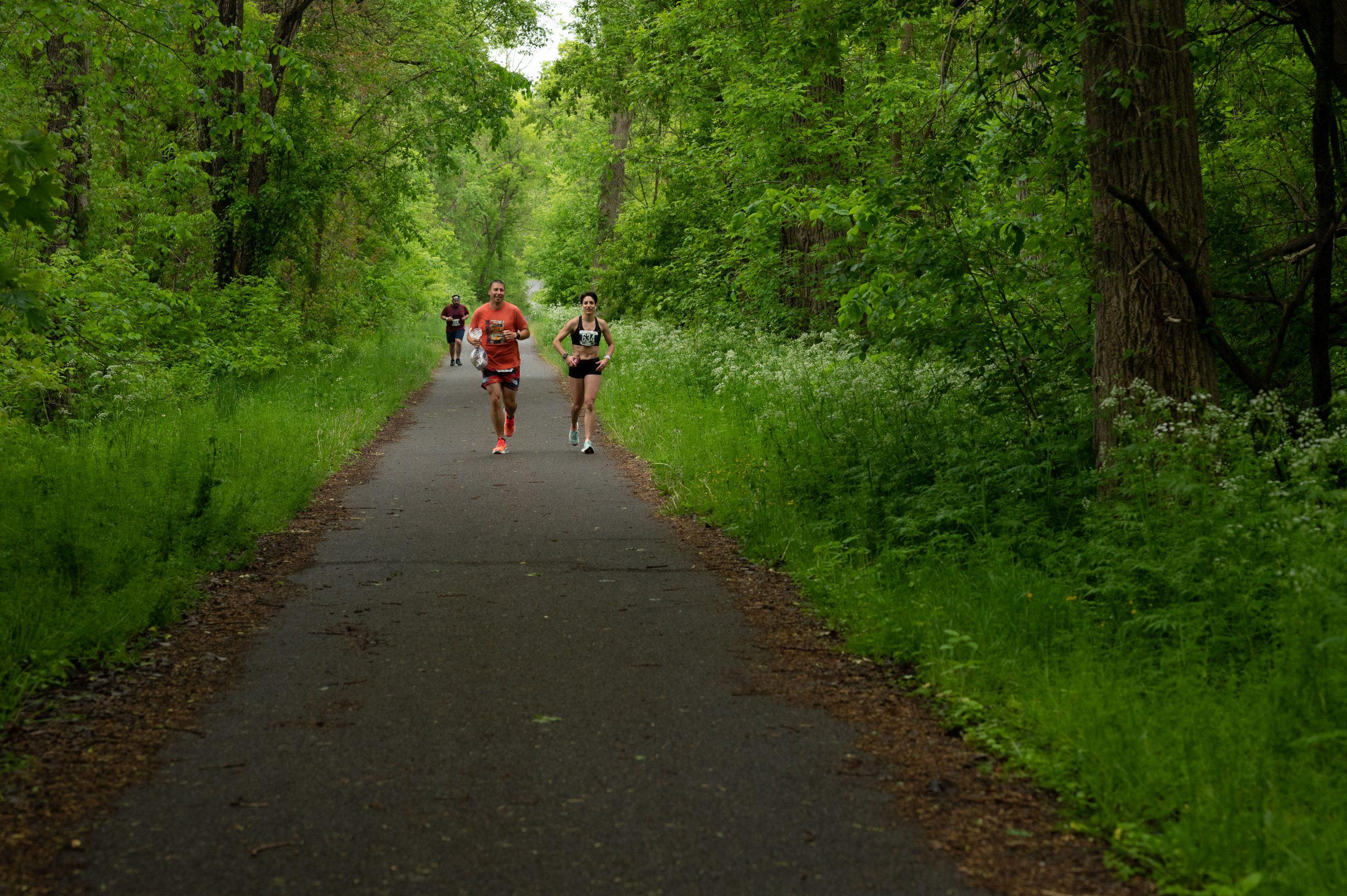 Two runners run down a tree-lined portion of the Erie Canal during the 2023 Erie Canal Races
