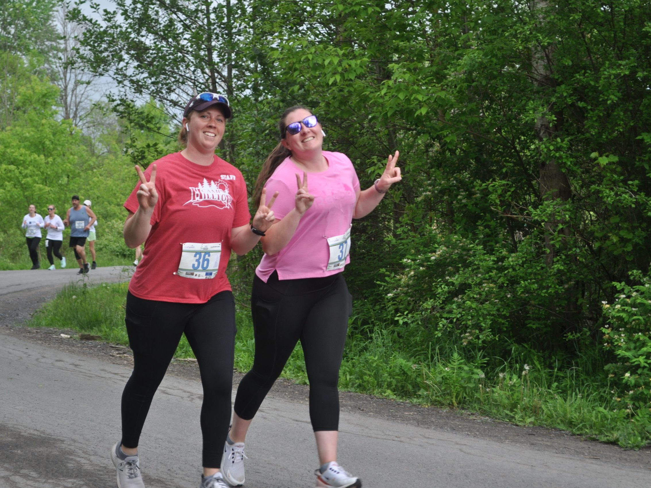 Two runners smile and give peace signs to the camera as running along the course of the Erie Canal Race
