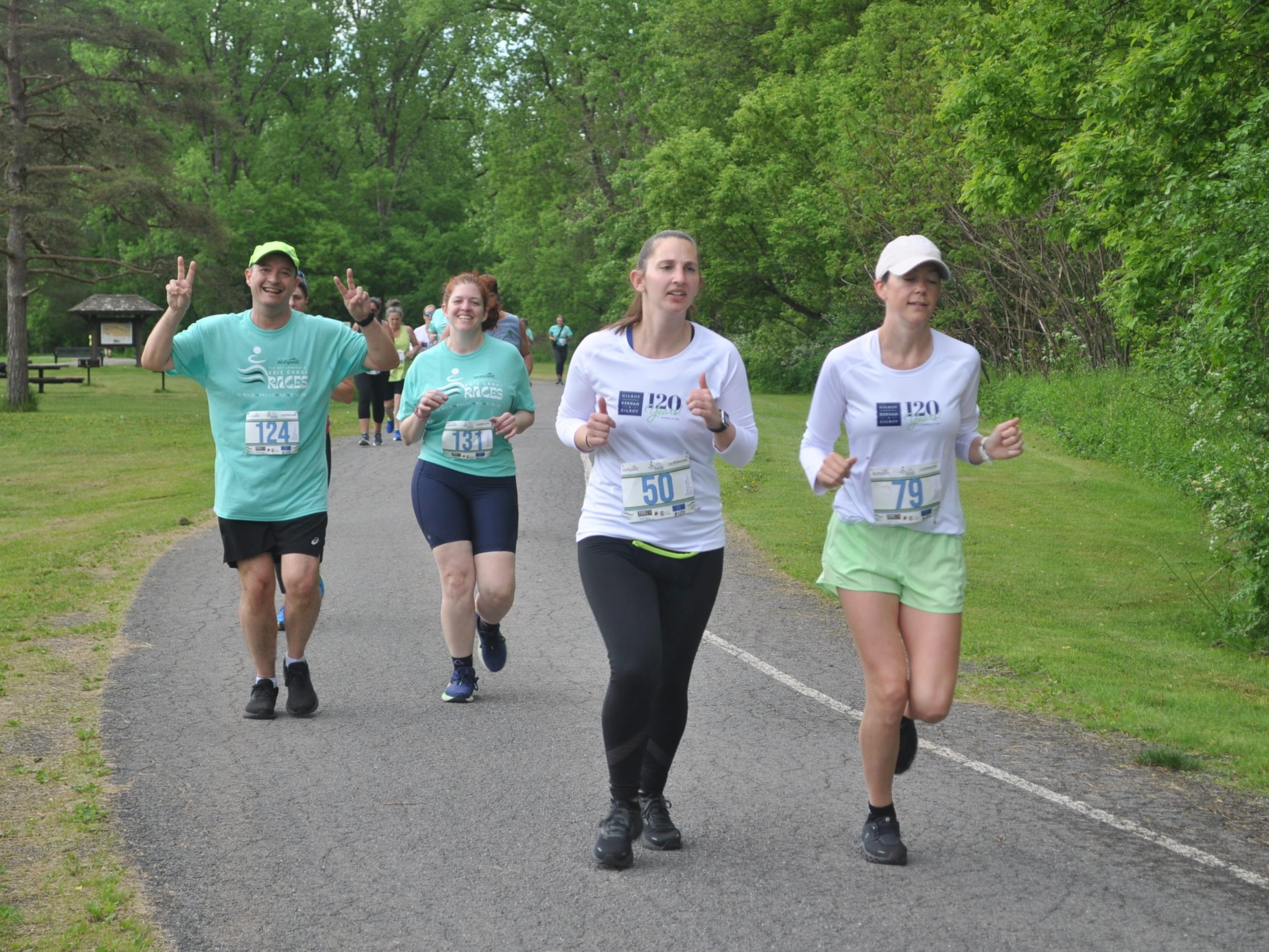Participants give peace signs and thumbs up as they run along the wooded course of the Erie Canal race