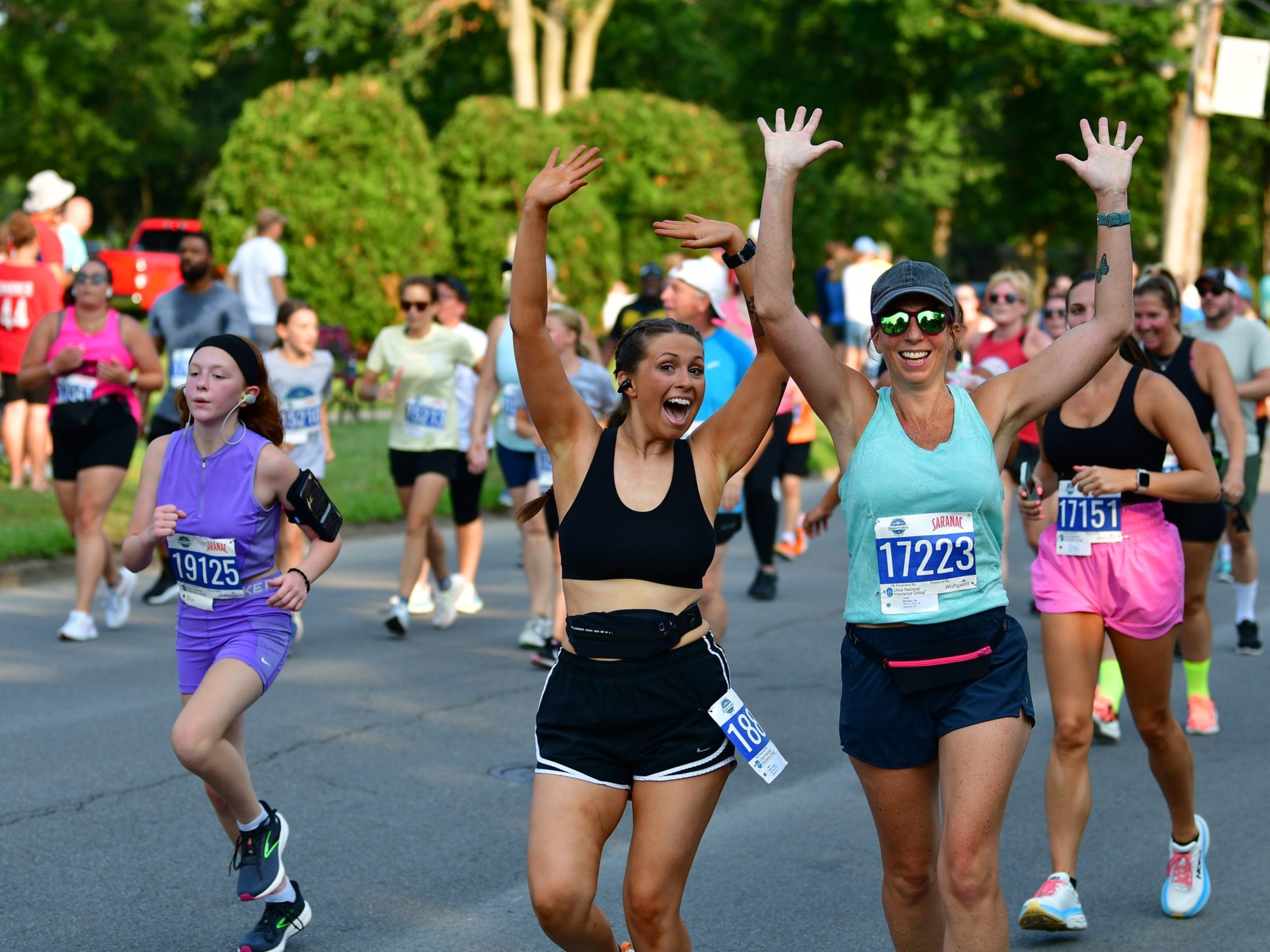Two participants hold up their hands and smile for the camera while running the Boilermaker 5K